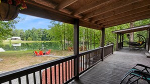 Une terrasse couverte avec vue sur un lac, une chaise et un pot de fleurs suspendu.
