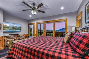 A bedroom with a large bed, a ceiling fan, a television, and a view of the outdoors through large windows. - Panoramic Pointe 2 Bedroom Cabin (Sevierville)