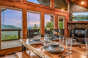 A dining area with a table set for four, large windows, and a stone fireplace.