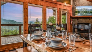 A wooden dining table set with plates, bowls, and glasses, overlooking a mountainous landscape through large windows. - Panoramic Pointe 2 Bedroom Cabin (Sevierville)