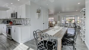 A modern kitchen with white cabinetry, a central island, and a dining area with a wooden table and metal chairs. - Luxury Pool Dog Friendly Central To Naples And Marco Island By Sky Run Naples 3 Bedroom Home (Naples)