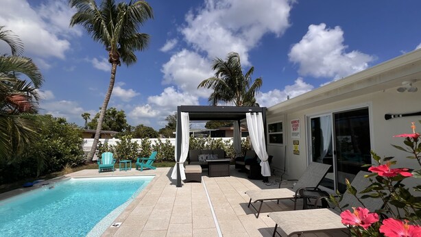 A pool area with lounge chairs, a covered seating area, and a clear blue sky. - Luxury Pool Dog Friendly Central To Naples And Marco Island By Sky Run Naples 3 Bedroom Home (Naples)