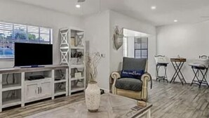 A spacious living room with a television on a white entertainment unit, a comfortable armchair, and a coffee table. - Luxury Pool Dog Friendly Central To Naples And Marco Island By Sky Run Naples 3 Bedroom Home (Naples)