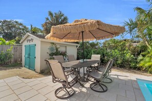 A patio with a table and chairs, a thatched umbrella, and a small shed with a green door. - Luxury Pool Dog Friendly Central To Naples And Marco Island By Sky Run Naples 3 Bedroom Home (Naples)