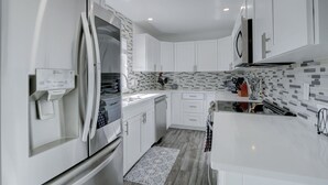A modern kitchen with white cabinetry, a built-in refrigerator, a microwave, and a tiled backsplash. - Luxury Pool Dog Friendly Central To Naples And Marco Island By Sky Run Naples 3 Bedroom Home (Naples)
