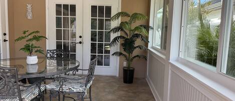 A dining area with a glass table and chairs, a potted plant, and a view of palm trees through a window.