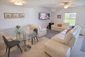 A living room with a glass table, two sofas, a TV, and framed pictures on the wall. - 2 Levels Pool Near Beach 2 Patios 2 Bedroom Apts (South Padre Island)