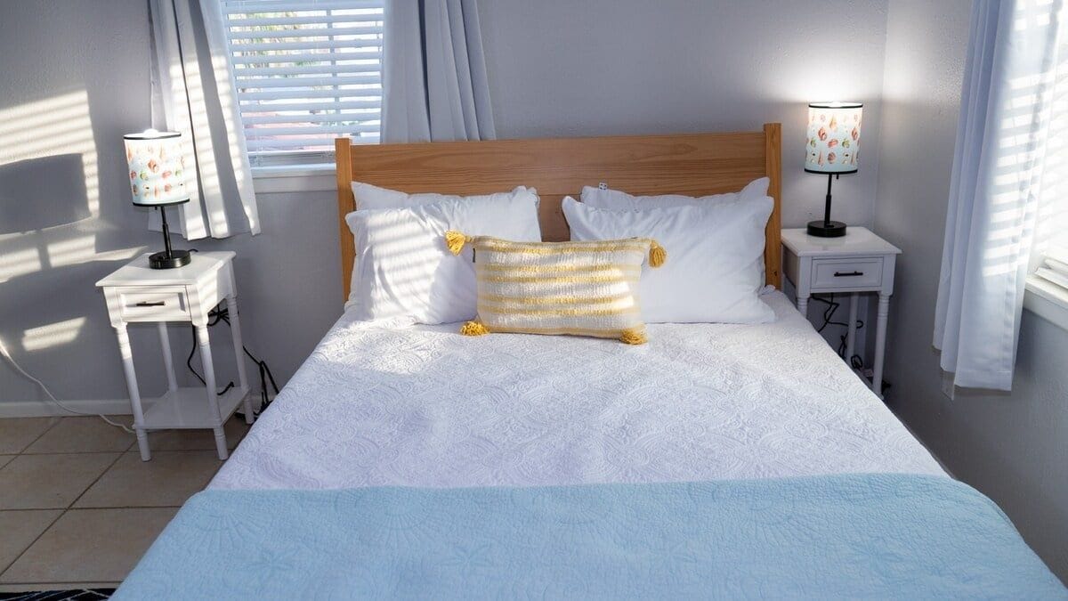 A bed with white bedding, two bedside tables with lamps, and a window with curtains.