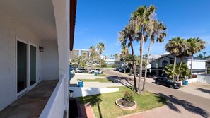 A residential area with a balcony, palm trees, parked cars, and a clear sky. - Fun Retro Island Vibe Sleeps 17 Beach 1 Block 4 Bedroom Home (South Padre Island)