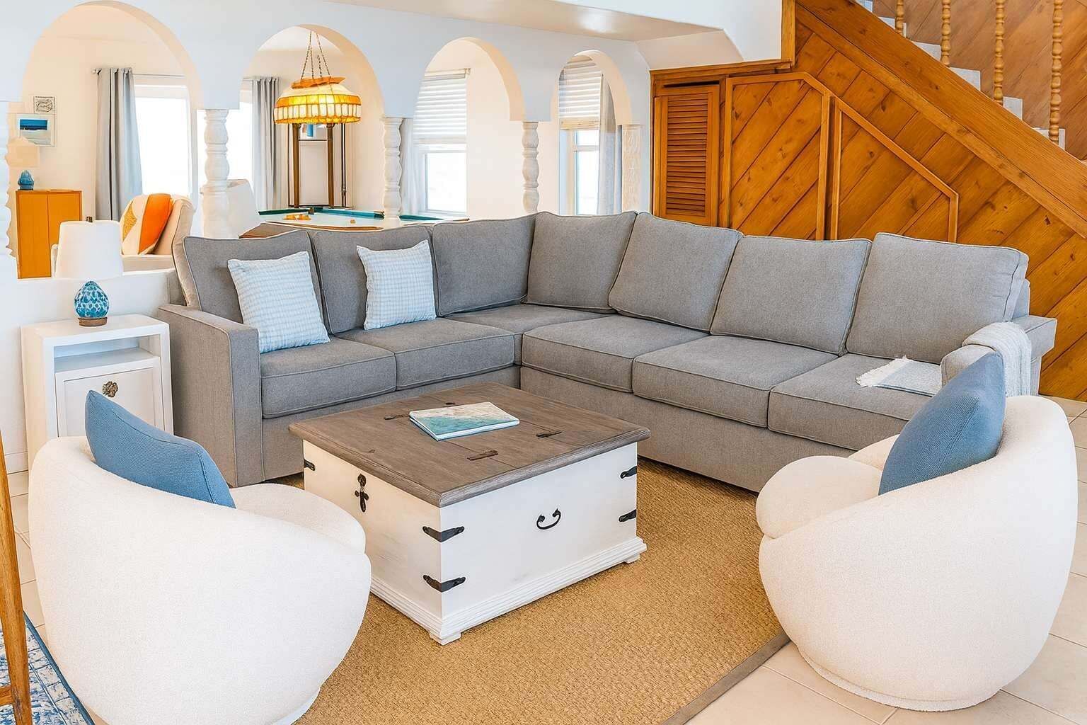 A modern living room with a grey sectional sofa, white armchairs, and a wooden coffee table.