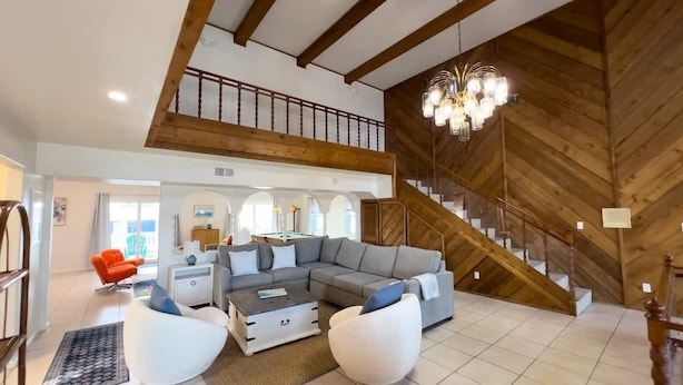 A spacious living area with a large gray sectional sofa, white armchairs, and a coffee table. A wooden staircase with a railing leads to an upper level. - Fun Retro Island Vibe Sleeps 17 Beach 1 Block 4 Bedroom Home (South Padre Island)