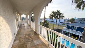 A covered balcony with a view of a swimming pool and a street.