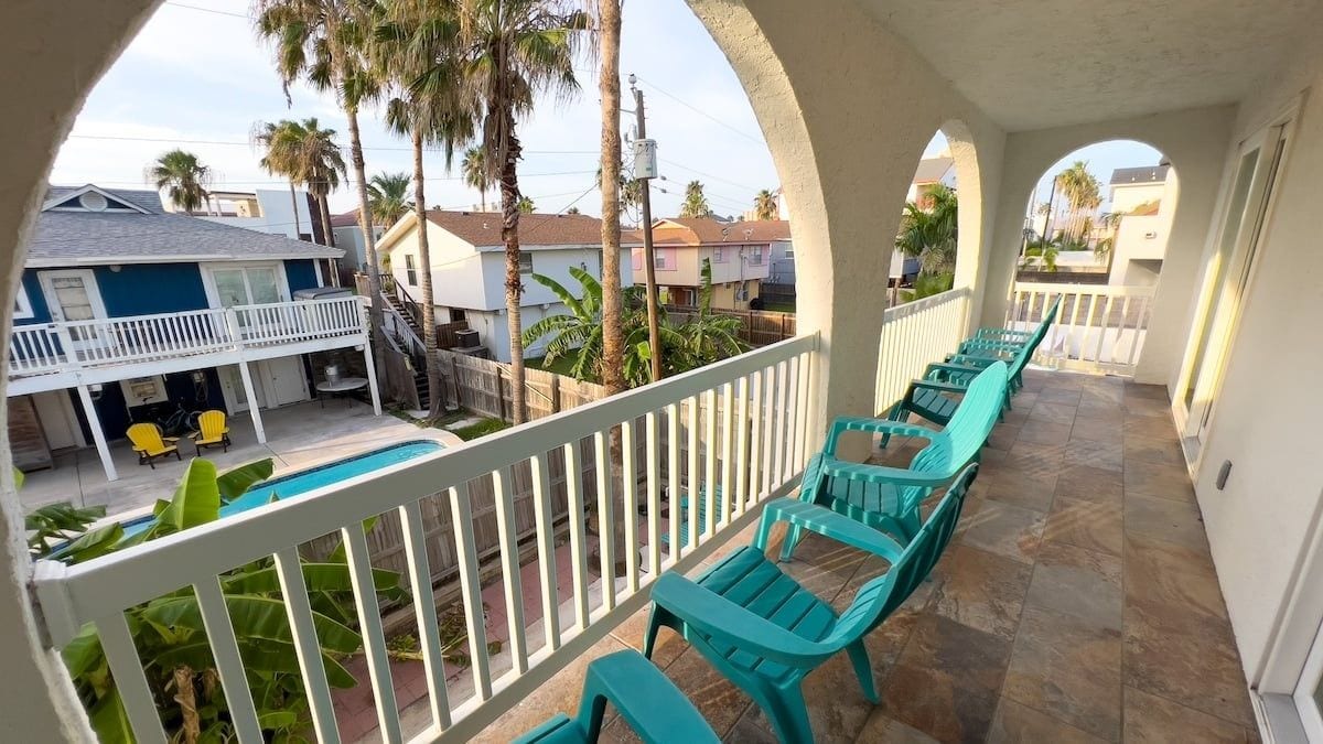 Een balkon met turquoise stoelen en een zwembad, omgeven door een witte balustrade.