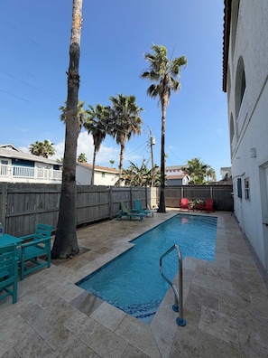 A swimming pool with a tiled deck, surrounded by palm trees and a wooden fence. - Fun Retro Island Vibe Sleeps 17 Beach 1 Block 4 Bedroom Home (South Padre Island)