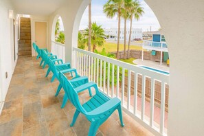 A covered balcony with turquoise chairs and a view of a pool and buildings. - Fun Retro Island Vibe Sleeps 17 Beach 1 Block 4 Bedroom Home (South Padre Island)