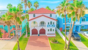 A two-story house with a red-tiled roof, a front porch, and a driveway leading to a garage. - Fun Retro Island Vibe Sleeps 17 Beach 1 Block 4 Bedroom Home (South Padre Island)