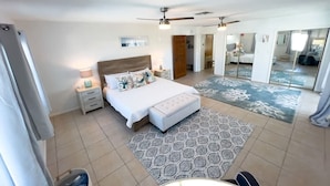 A bedroom with a bed, bedside tables, a ceiling fan, and a large mirror. - Fun Retro Island Vibe Sleeps 17 Beach 1 Block 4 Bedroom Home (South Padre Island)