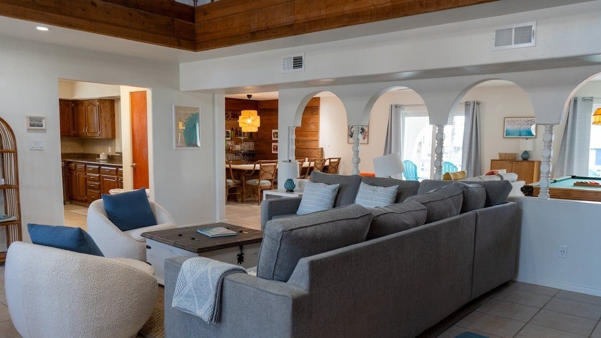 A spacious living area with a sofa set, a coffee table, and a dining area visible through an archway.