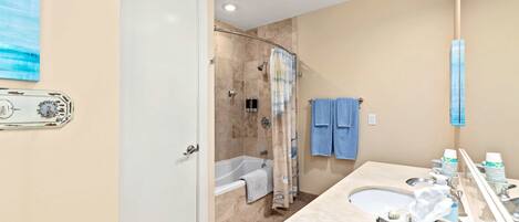 A bathroom with a bathtub, shower, and sink. There are towels hanging on the wall and a mirror above the sink.