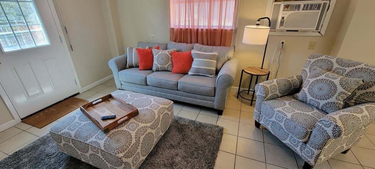 A living room with a grey sofa, patterned ottoman, and patterned armchair.