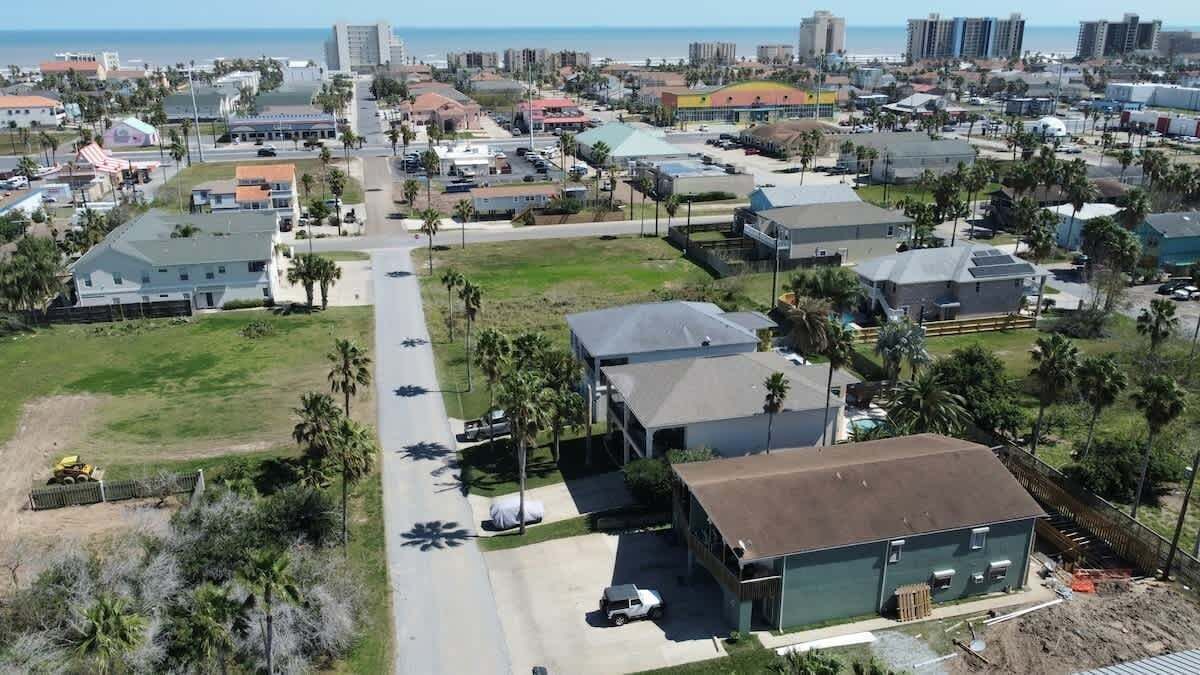An aerial view of a residential area with houses, roads, and a beach in the background.