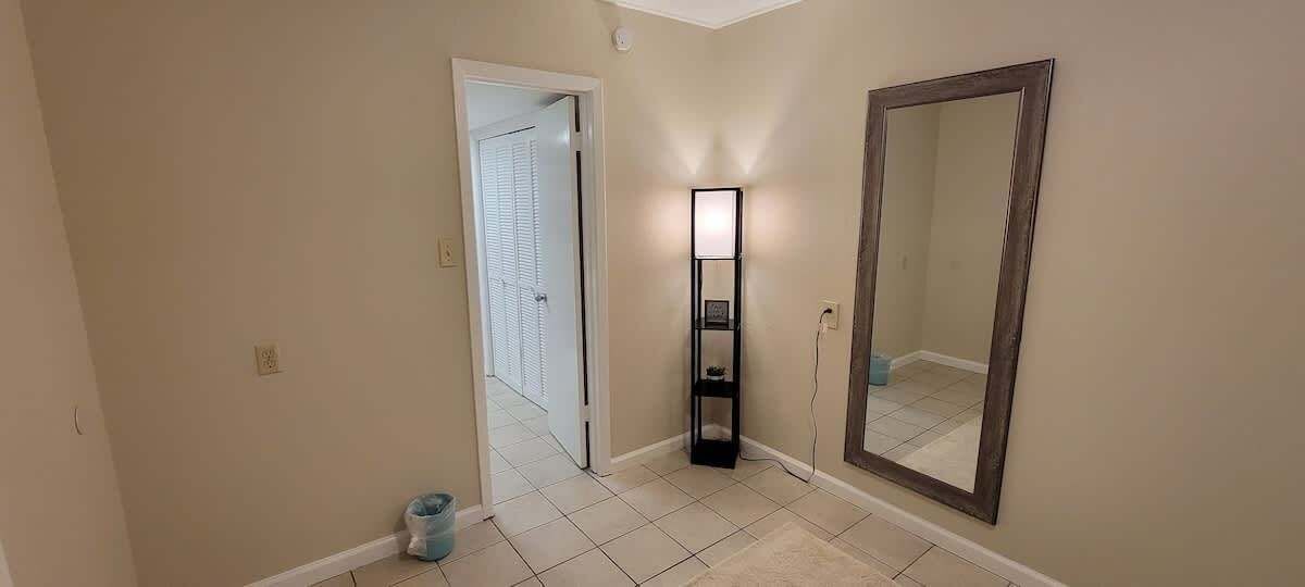 A hallway with a light fixture, a mirror, and a door leading to another room.