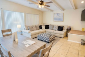 A modern living room with a beige sofa, a wooden dining table, and a ceiling fan.