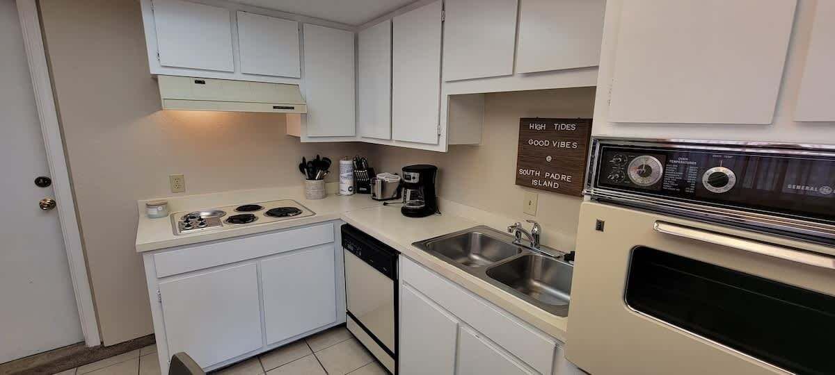 Una cocina compacta con armarios blancos, estufa, lavabo y horno antiguo.