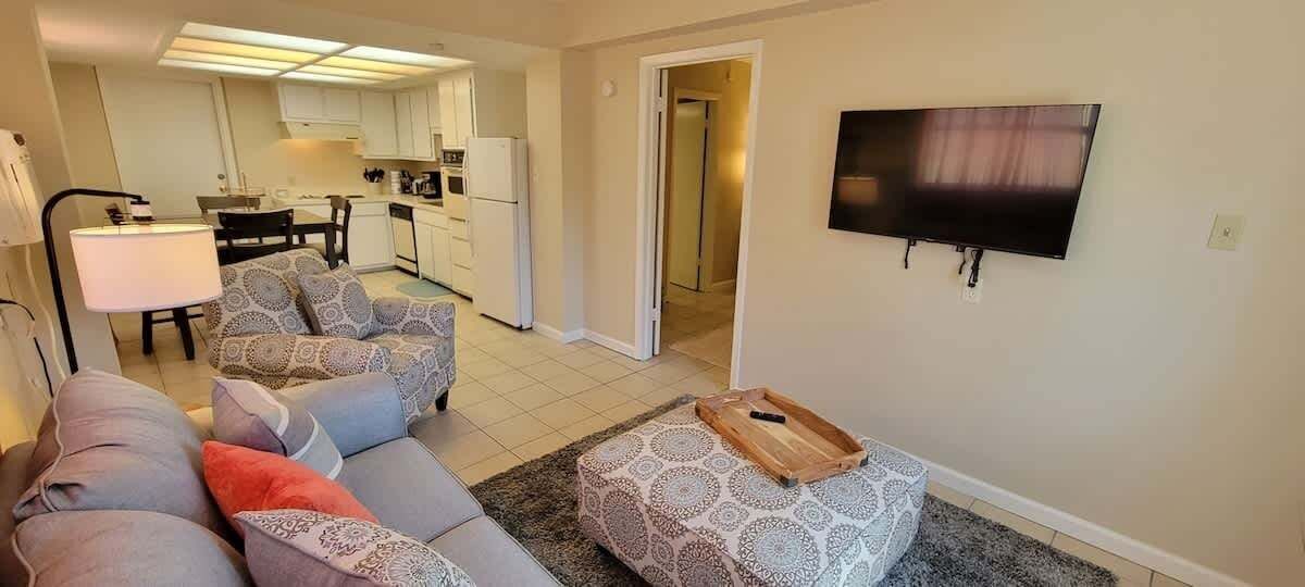 Un salon comprenant un canapé, un pouf et un téléviseur à écran plat fixé au mur.