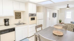 A compact kitchen with white cabinets, a dishwasher, a coffee maker, and a dining area with a wooden table and chairs.