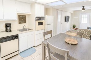 Une cuisine compacte avec des meubles blancs, un lave-vaisselle, une machine à café et un coin repas comprenant une table et des chaises en bois.