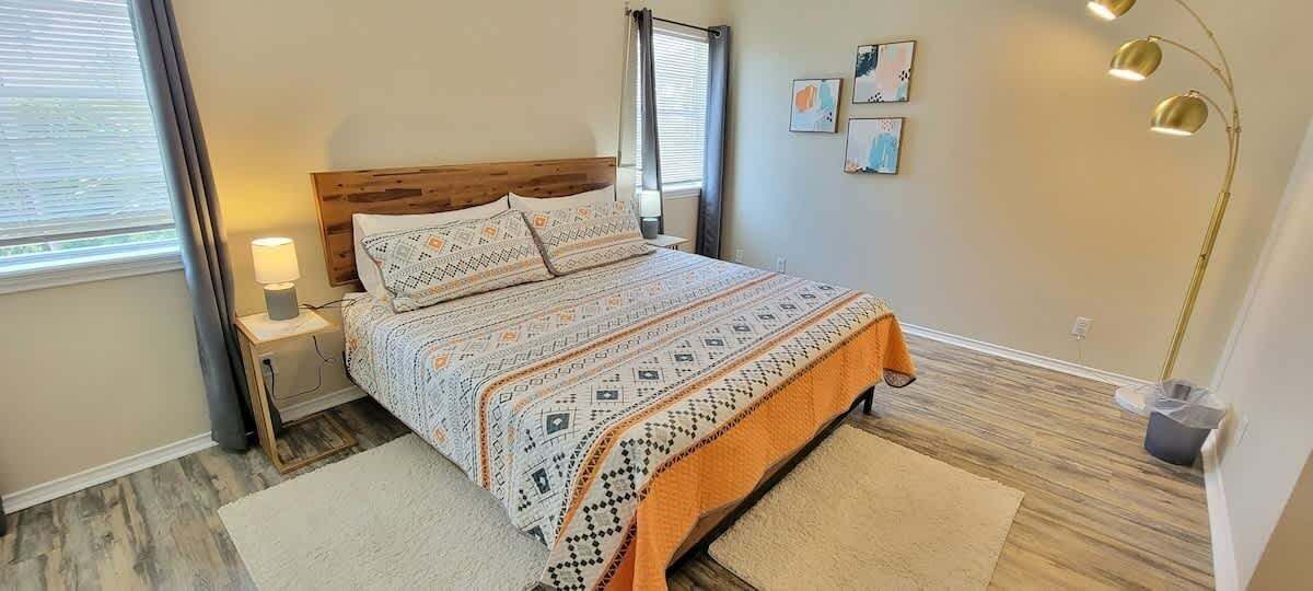 A bedroom with a bed, nightstands, a lamp, and artwork on the wall.