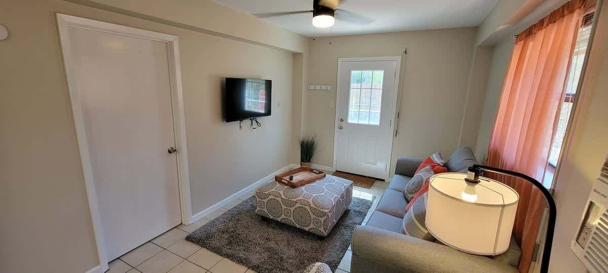 A compact living room with a sofa, a coffee table, a TV mounted on the wall, and a door leading to another room.