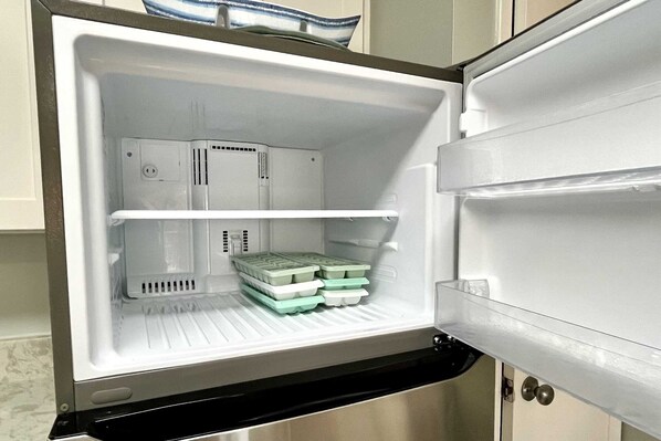 An open refrigerator with two shelves, one containing green containers and the other empty.