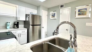 A modern kitchen with white cabinets, a stainless steel refrigerator, a double sink, and a coffee maker.