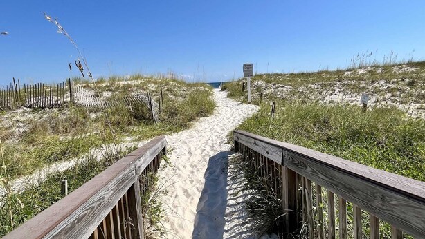 A sandy beach path with wooden railings, leading to the ocean.