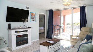 A living room with a flat-screen TV, a fireplace, a sofa, and a balcony with outdoor furniture.