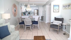 A spacious living area with a dining table, chairs, a sofa, and a kitchen in the background.