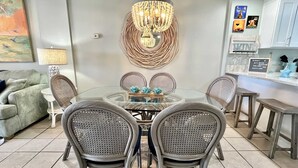 A dining area with a glass table and wicker chairs, a chandelier, and a wall-mounted light fixture.