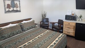 A bedroom with a bed, a desk, a chair, a microwave, and a television. - South of the Border VT Room 1 (Canaan)