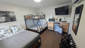 A compact room with two bunk beds, a small kitchenette, and a flat-screen TV mounted on the wall.