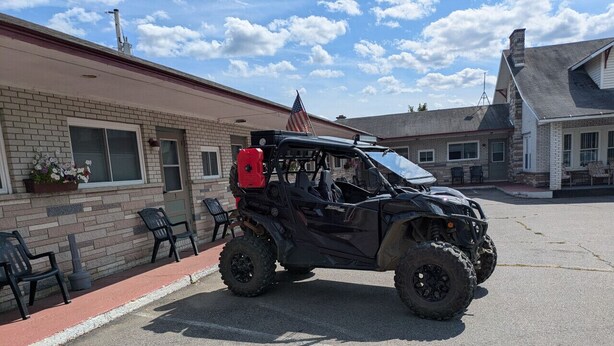 A black off-road vehicle parked in front of a building with a brick facade, a red awning, and outdoor seating.