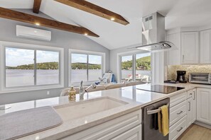 Une cuisine dotée d’un grand îlot central, de meubles blancs et offrant une vue sur un lac.