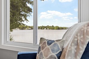 A room with a large window overlooking a body of water, a blue chair, and a patterned pillow.