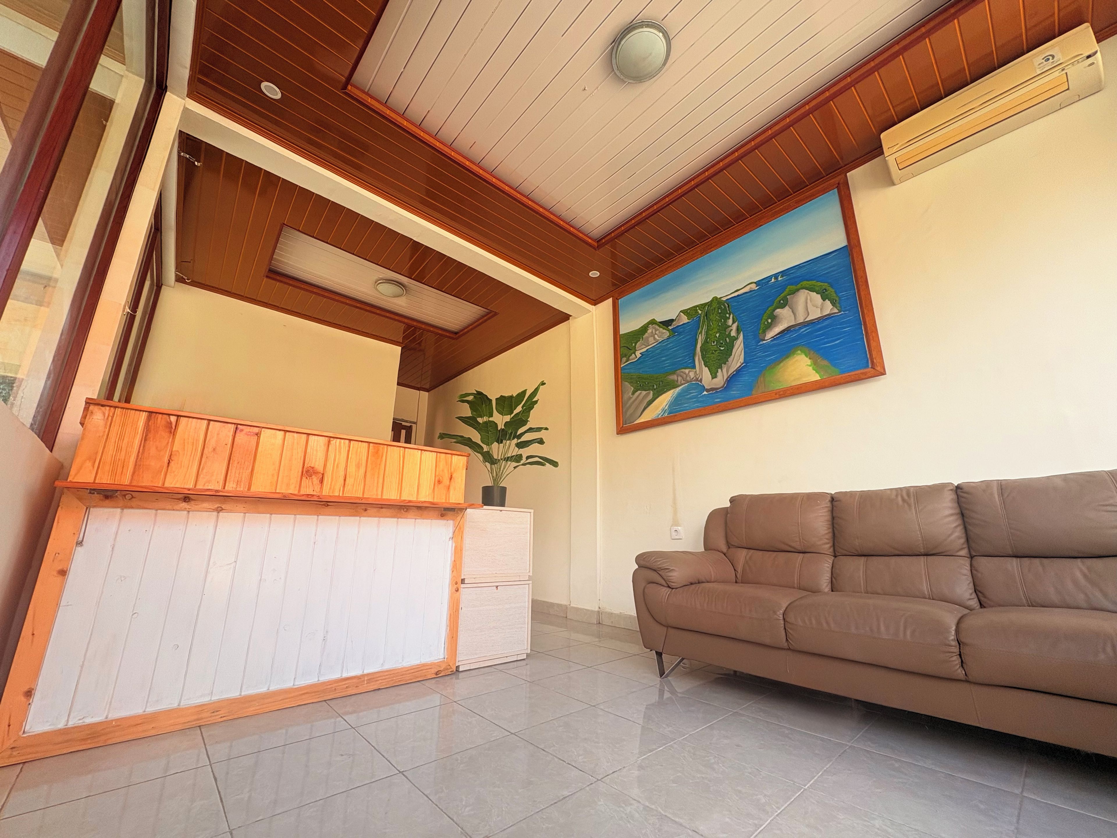 Un área de recepción con un mostrador de madera, un sofá de cuero marrón y un cuadro de un paisaje costero en la pared.