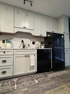 Una cocina con armarios blancos, un refrigerador negro y un piso de madera con diseño de cocina.