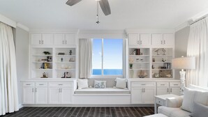 Una sala de estar moderna con un banco empotrado, armarios blancos y vista al mar.