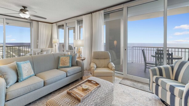 Un balcón amplio con sofá, sillón y una silla a rayas, con vistas al océano.