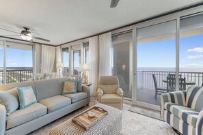 A spacious balcony with a sofa, armchair, and striped chair, offering a view of the ocean.