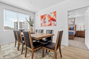 A modern dining area with a wooden table and chairs, a large window with blinds, and a city view.